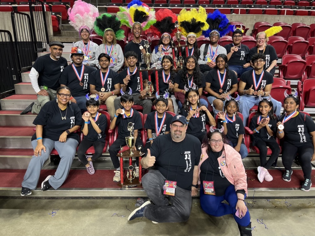 NJ Odyssey of the Mind teams sand volunteers at Iowa State showing off their Odyssey World Finals awards. The people are sitting in auditorium style folding chairs and dressed in their NJOOTM t-shirts.