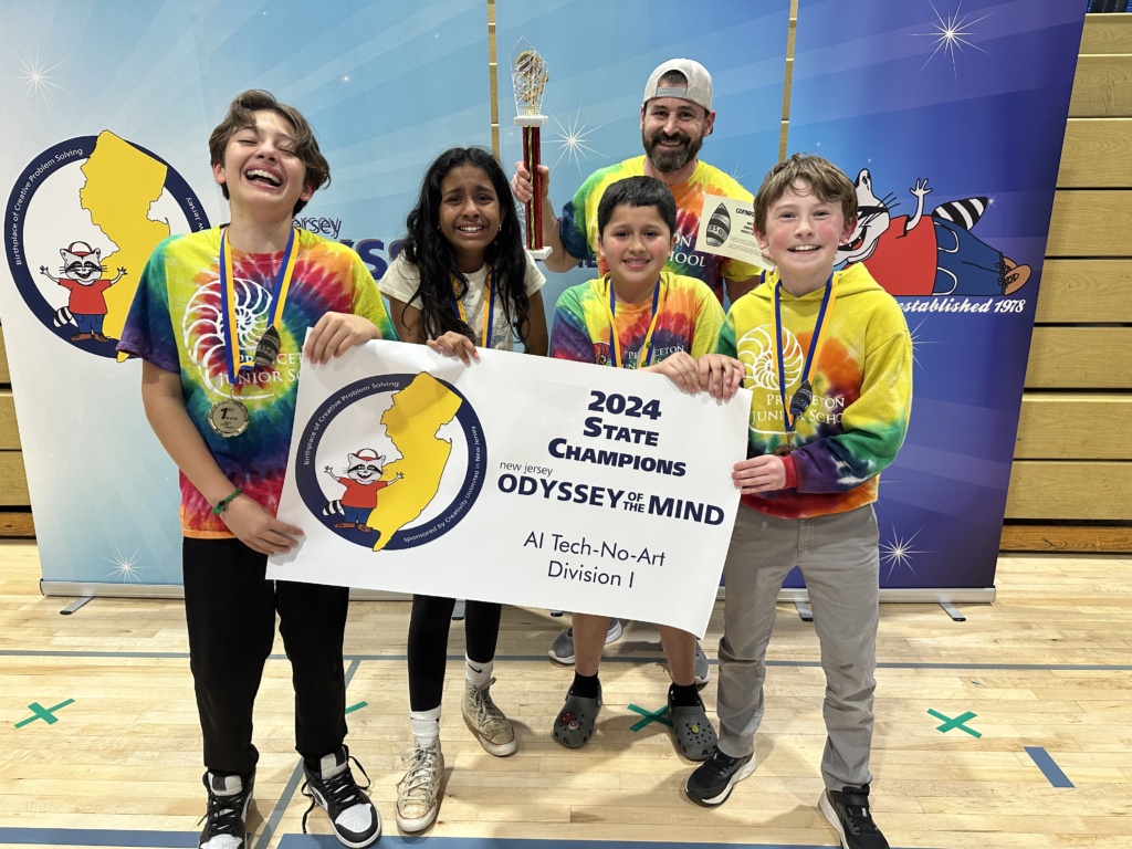 Four children and a teacher in tie dyed shirts holding their 350 Awards Banner. 